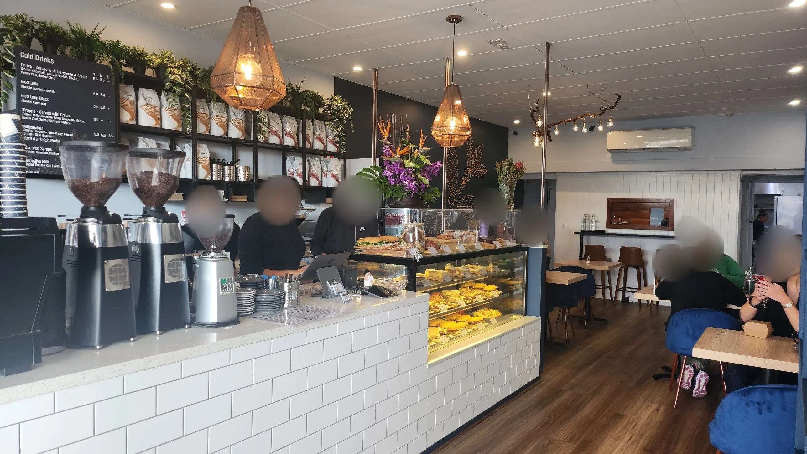 Inside the Melbourne café: the counter, coffee grinders and cabinet, with customers at the tables.