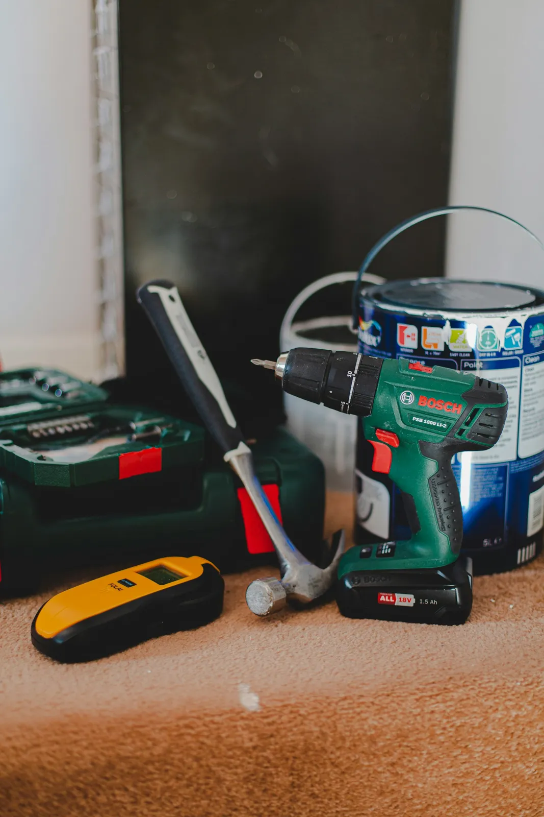 A cordless drill, hammer and stud finder laid out on a bench.